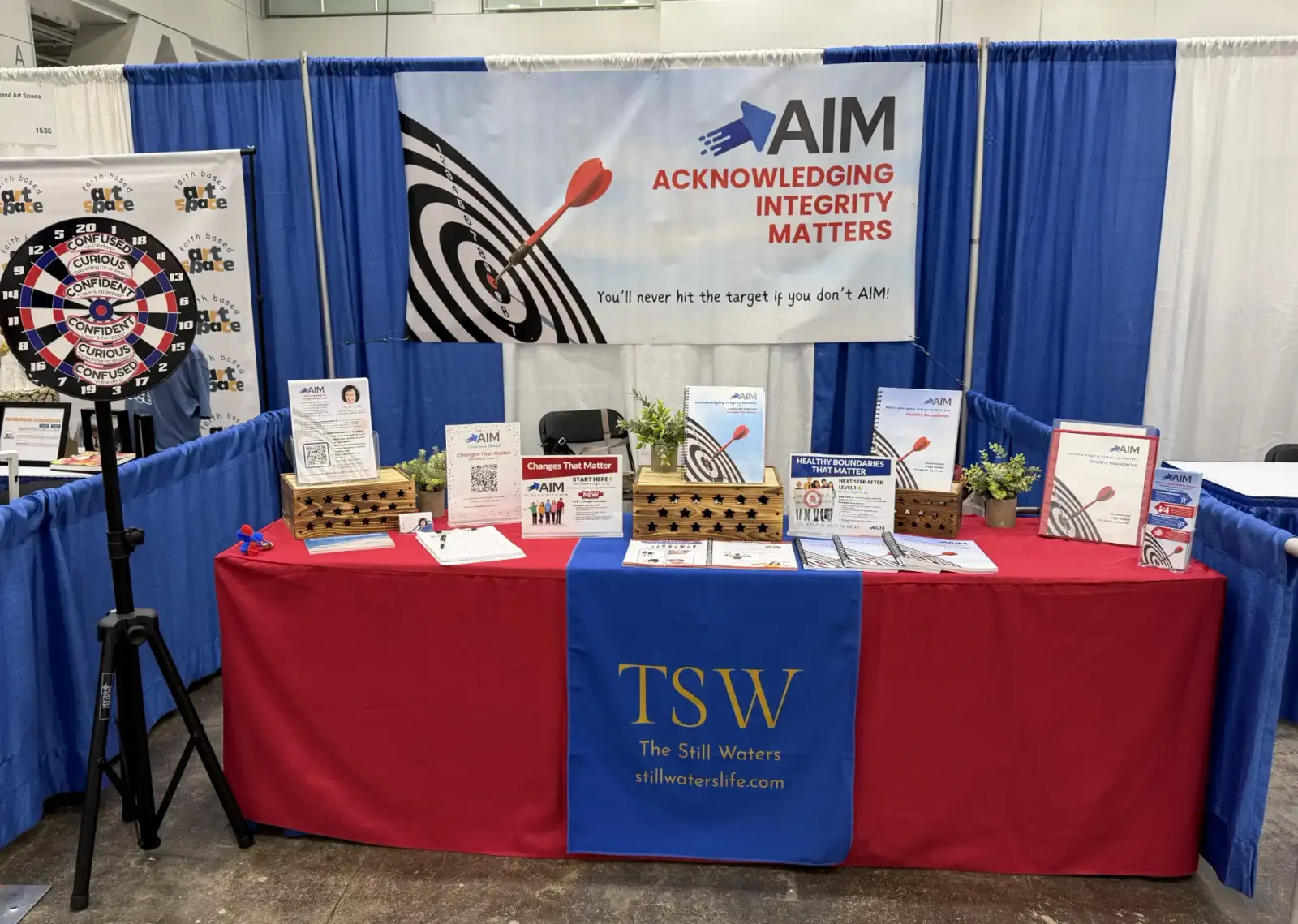 The AIM exhibit booth setup at a homeschool conference, featuring the AIM target banner and curriculum materials
