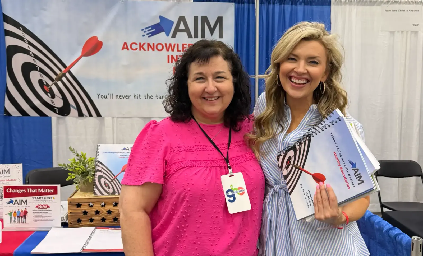 Teri White with a fellow presenter at the AIM booth, holding AIM Healthy Boundaries student journals
